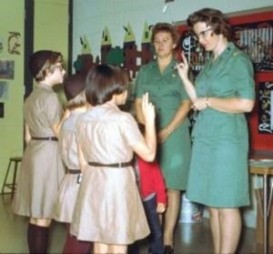 An old color photo of three young girls and two adult women in old-fashioned Girl Scout uniforms